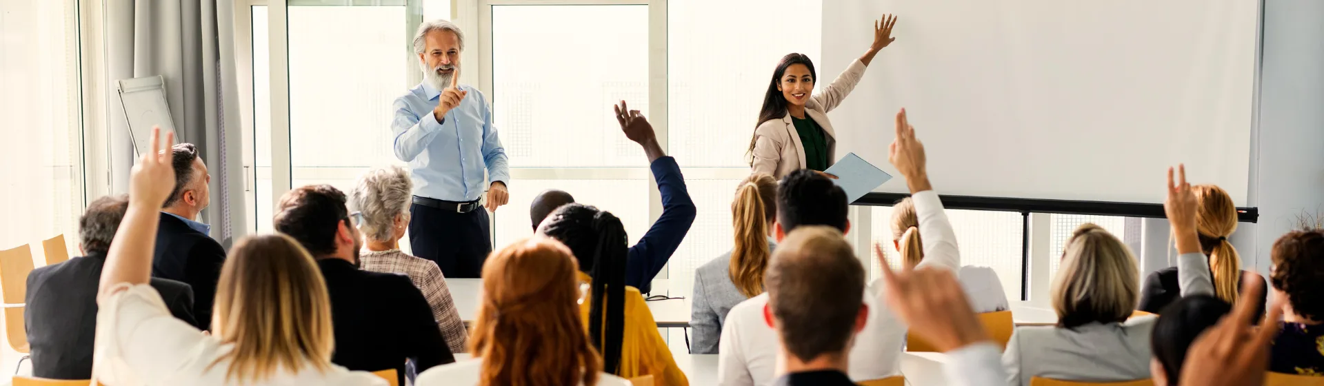 Oktató előadást tart egy tanteremben, a hallgatók jelentkeznek